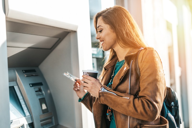 woman holding coffee smiling contently as she uses her Members Heritage debit card at an ATM